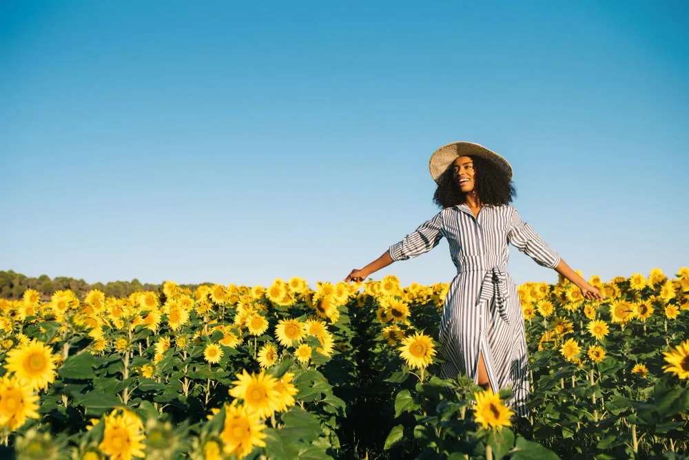 Woman in sundress and sunhat walking through a field of sunflowers on a clear day